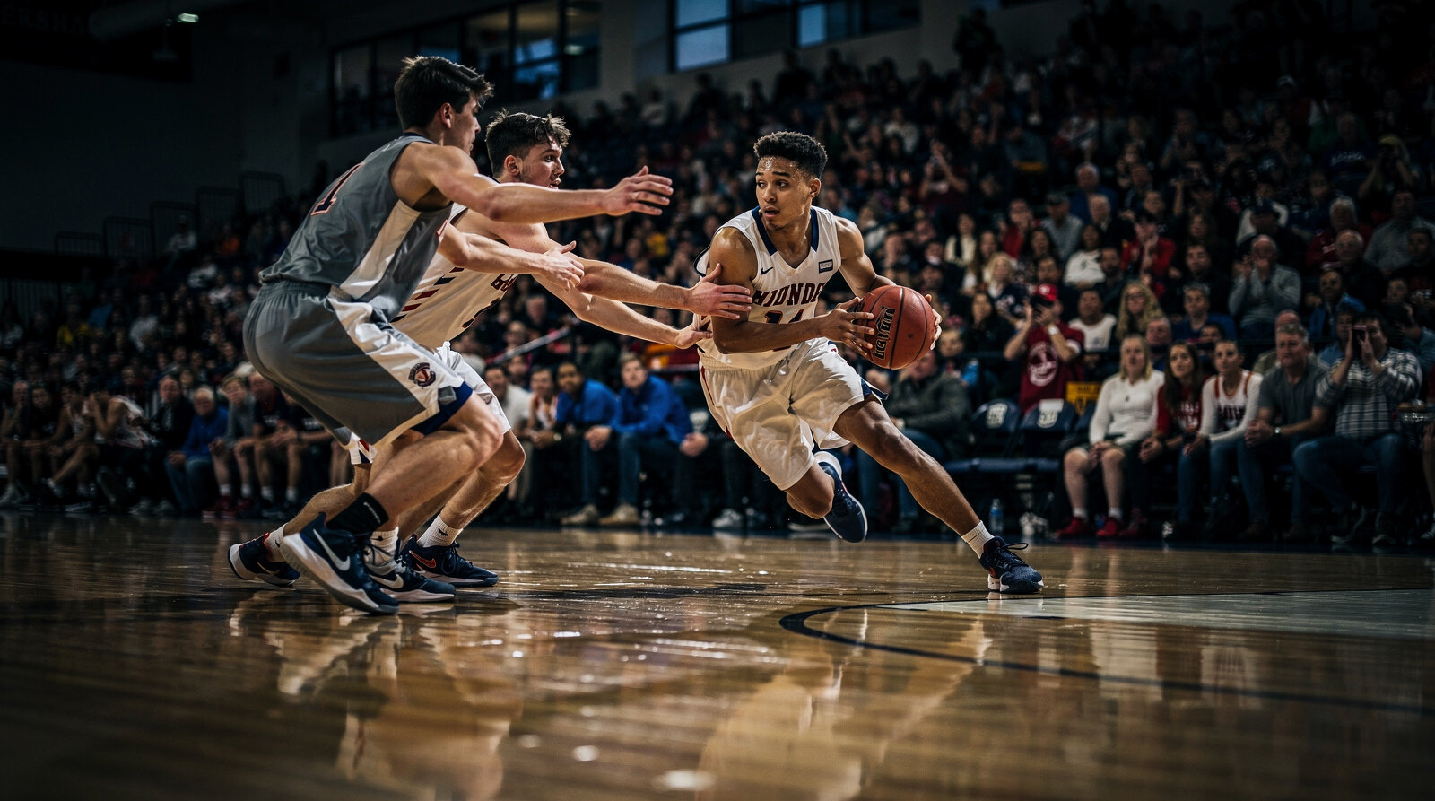 Guard driving baseline past two defenders in front of a packed crowd