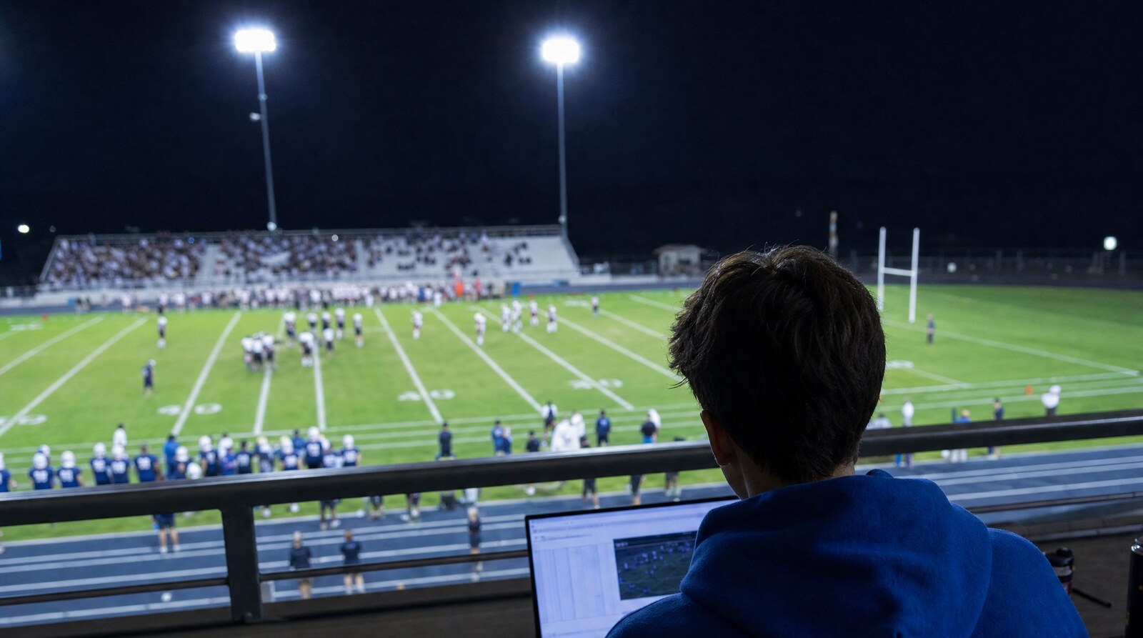 Scorer working a Friday night football game from the press deck, laptop open to a live stat sheet